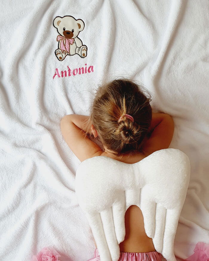 Playful young girl observes cute teddy bear on her personalized blanket